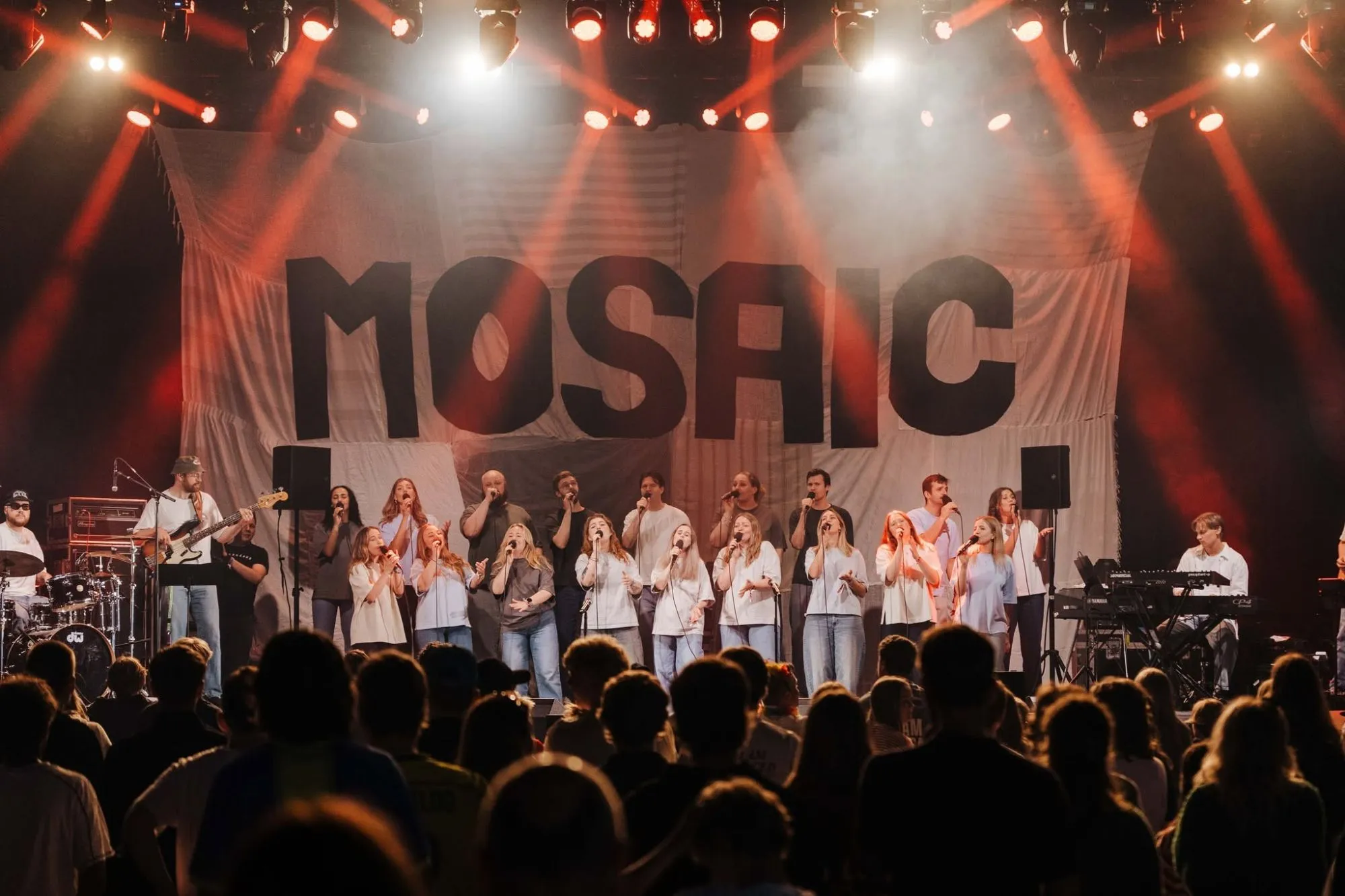 Mosaic synger med band på en stor scene foran et banner med navnet Mosaic, med publikum i forgrunnen